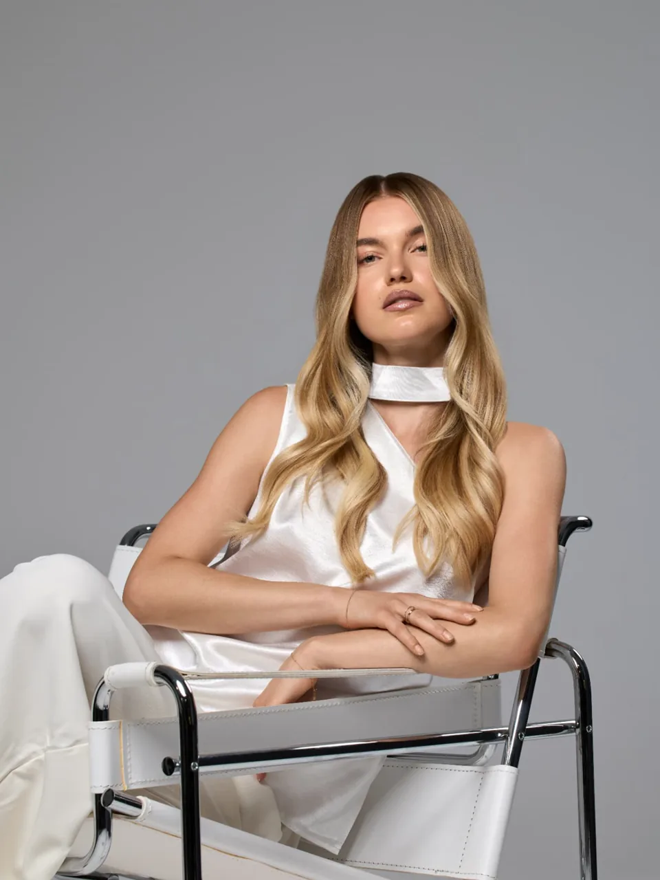 Eine Kundin mit blondem Haar sitzt in einem Stuhl mit Metallgestell und blickt in die Kamera.